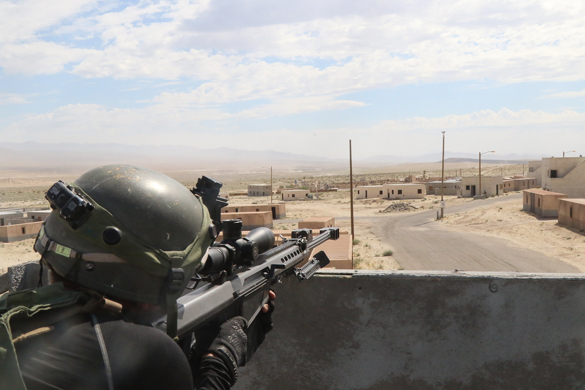 A soldier surveys the battlefield with a simulated Barrett M107 .50 caliber sniper rifle on July 12, 2019, in the city of Razish at the National Training Center at Fort Irwin, Calif.